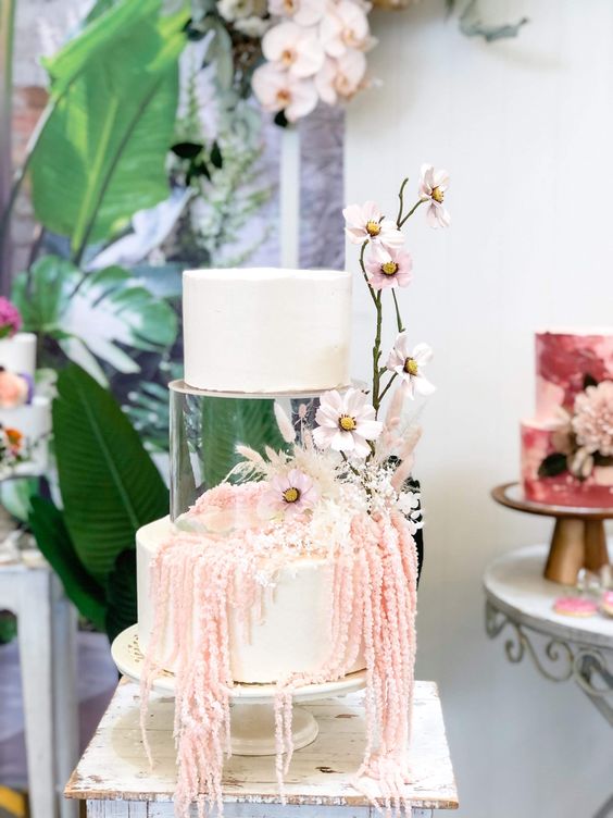 a white wedding cake with a clear acrylic tier decorated with pink blooms and blooming branches on the outside