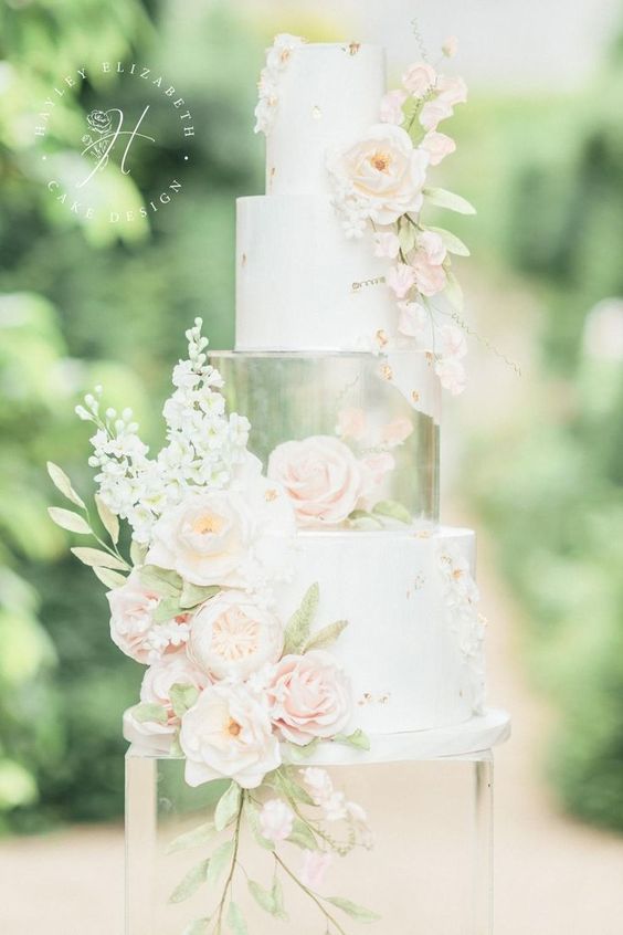 a white wedding cake with a clear acrylic tier with a pink bloom and some pink blooms on the outside is amazing
