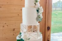 a white wedding cake with an acrylic separator with geometric decor, white blooms and greenery and a gold calligraphy topper