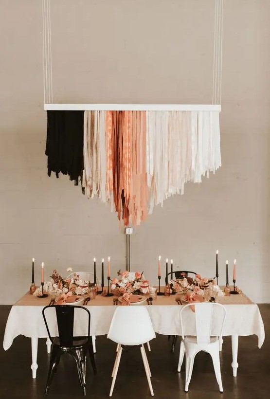 an edgy wedding reception space with a black, nude and coral streamer chandelier, matching candles and black and white chairs