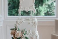 an elegant and refined white square wedding cake with white sugar blooms, fresh blush ones and greenery and a clear acrylic separator