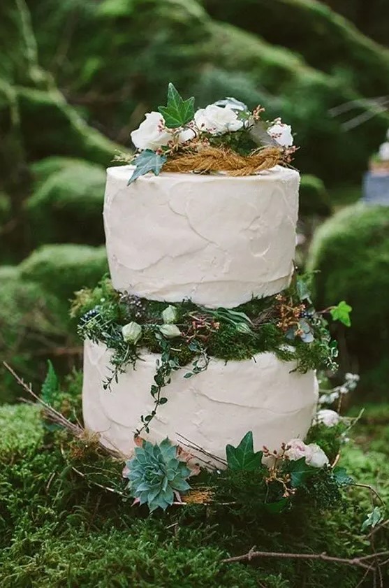 an enchanted forest wedding cake with textural white tiers, moss, greenery, white blooms and leaves plus succulents looks dreamy