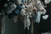 an exquisite moody floral wedding installation with white, blush and mauve and black blooms and leaves plus ribbons is wow