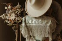 02 a bleached denim jacket with letter applique and silver fringe, a neutral hat are perfect accessories for a boho bride