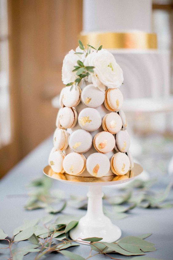a neutral macaron tower cake with gold foil and white blooms and greenery on top is a very chic and refined idea