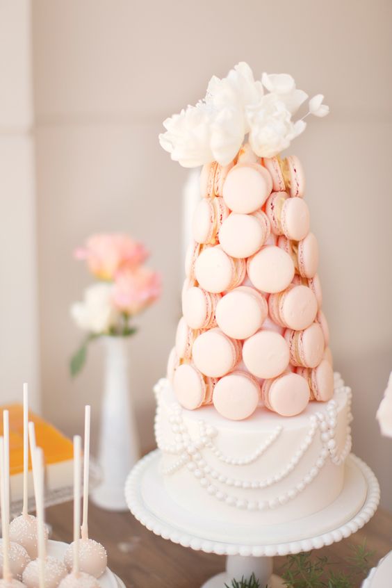 a refined white wedding cake decorated with edible pearls and blush macarons plus white blooms on top is very sophisticated