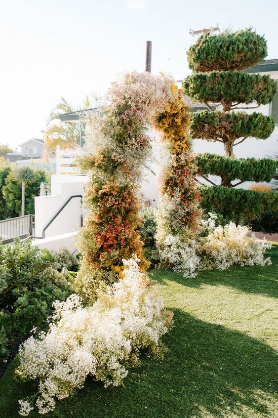 a lovely and creative baby's breath wedding arch spray painted in various colors, with additional blooms on both sides