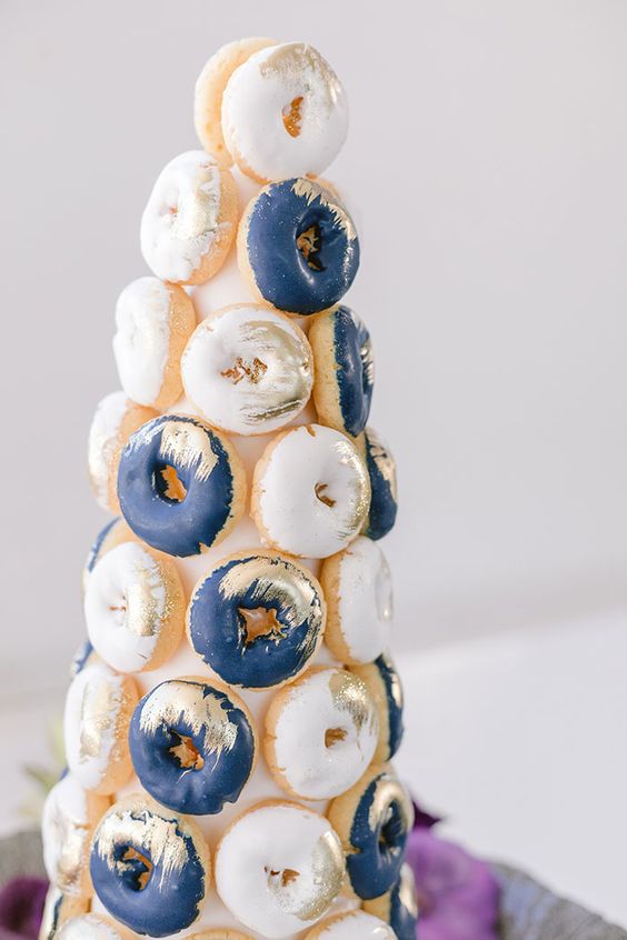 a lovely white and navy glazed donut tower with gilded touches is a chic and bold idea for a modern wedding