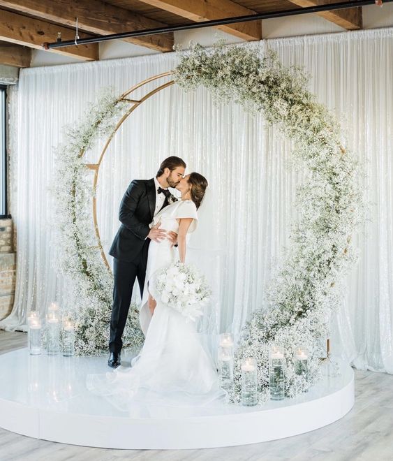 a round wedding arch decorated with white baby's breath and with floating candles in tall glasses for a modern wedding