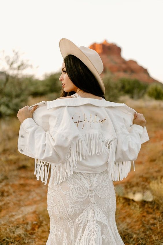 a white denim jacket with gold calligraphy and white fringe is a cool idea for a boho bride, add a hat and go