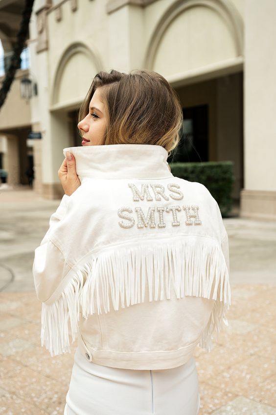a white denim jacket with embellished letters and long fringe is a perfect addition to a boho bridal look
