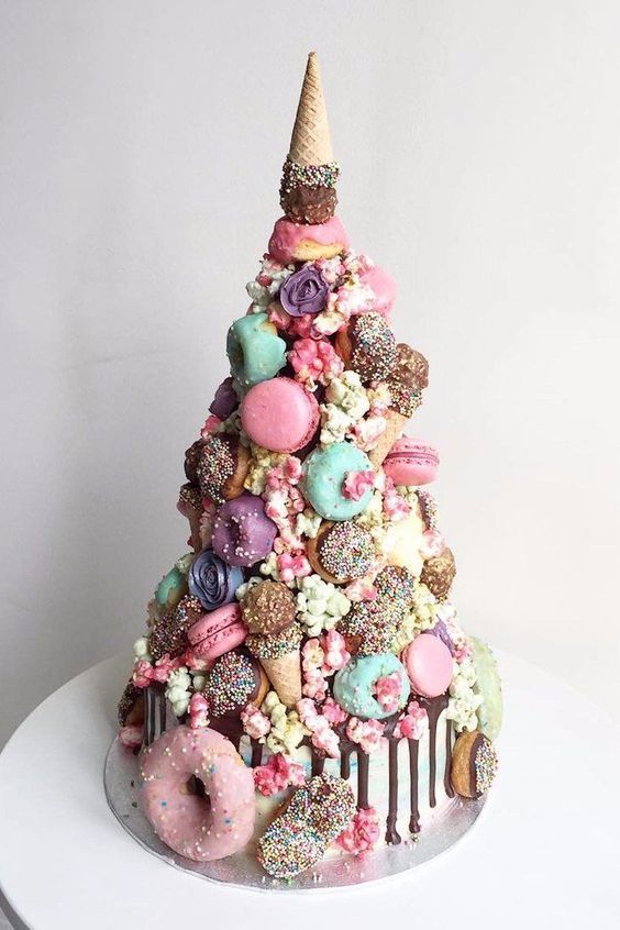 a colorful and whimsical wedding cake with chocolate drip, bright and pastel macarons, glazed donuts, candies and ice cream cones