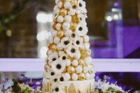 23 a gilded wedding cake with creamy drip, with a croquembouche tower with chocolate, white anemones is very whimsical