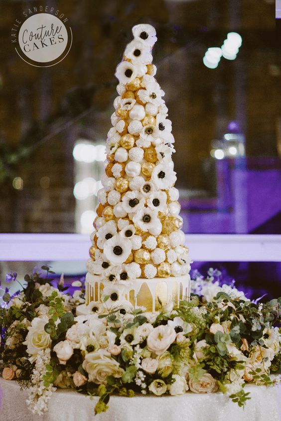a gilded wedding cake with creamy drip, with a croquembouche tower with chocolate, white anemones is very whimsical