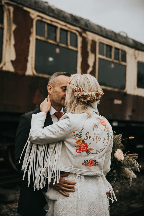 a white cropped leather jacket with long fringe on the sleeves, painted blooms and calligraphy is a cool idea for a boho bride