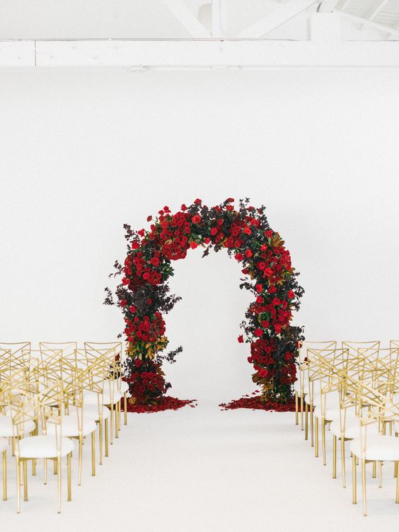 a refined wedding ceremony space with gold and white chairs and a green and red rose wedding arch that makes a statement