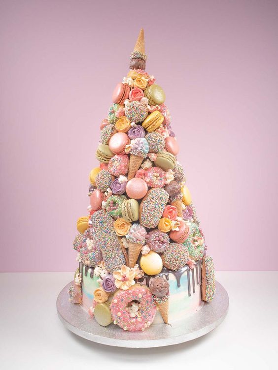 a quirky pastel wedding cake with chocolate drip, macarons, glazed donuts, ice cream cones and edible blooms