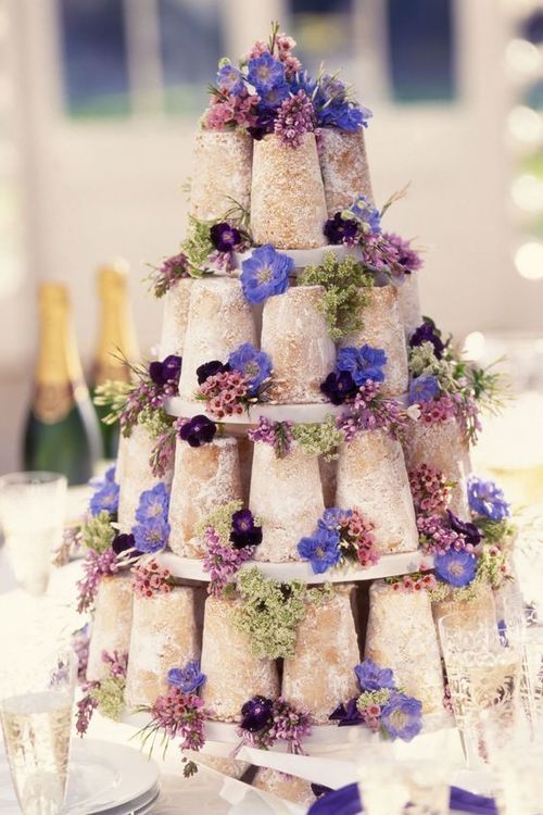 a tower of mini naked wedding cakes decorated with lilac, violet and deep purple blooms and greenery for a relaxed wedding