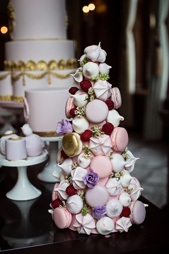 a chic and refined tower wedding cake that consists of pink and neutral macarons, meringues, gilded macarons, lilac blooms and meringues