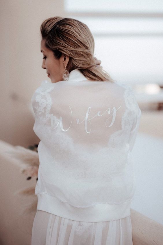 a sheer white bridal bomber with white calligraphy is a very chic and sophisticated idea for a modern bride