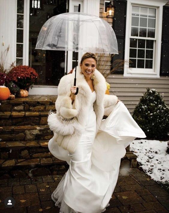 a glam bridal outfit with a strapless mermaid wedding dress, a white faux fur jacket and statement earrings for a winter celebration