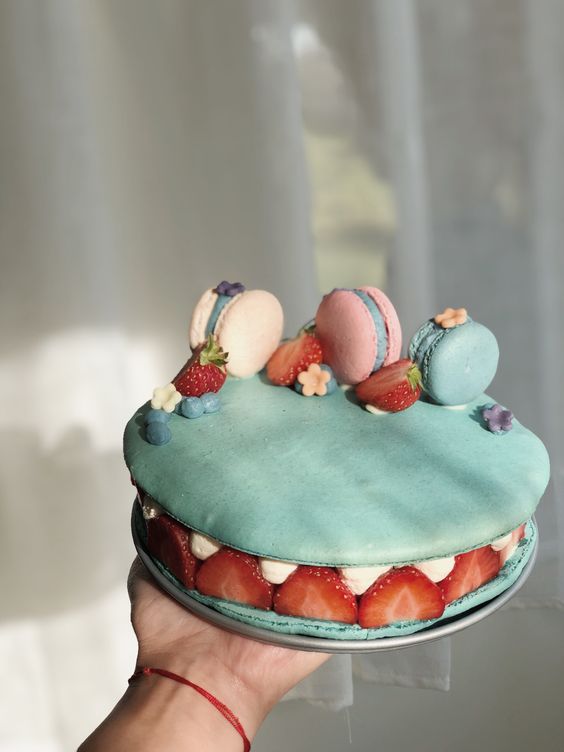 a blue macaron cake with vanilla cream, strawberries and pastel colored macarons on top is an amazing idea