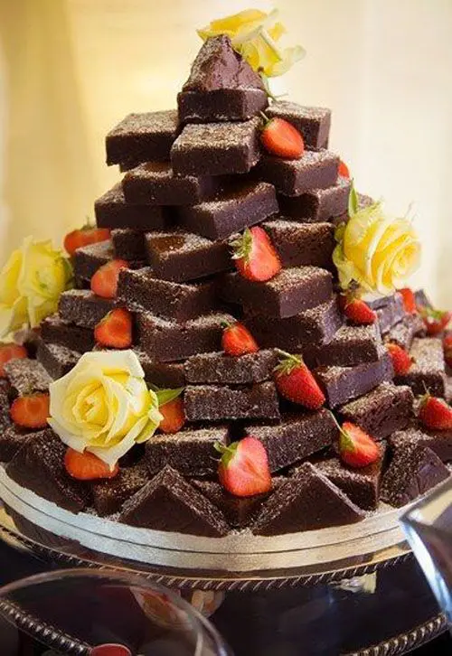a brownie stack decorated with yellow roses and topped with strawberries is a perfect solution for a wedding