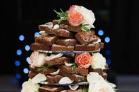 a brownie wedding cake decorated with greenery, coral and white blooms placed on a tree slice is a timeless idea for a rustic wedding