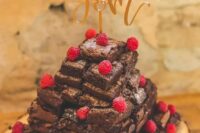 a brownie wedding cake topped with fresh raspberries and with a gold calligraphy cake topper is a sophisticated solution