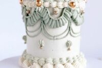 a chic pale green lambeth wedding cake with white and green sugar detailing, with gold beads and some candles on top