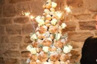 a cool croquembouche wedding cake topped with sugar powder, white roses, greenery and sparklers for a NYE wedding