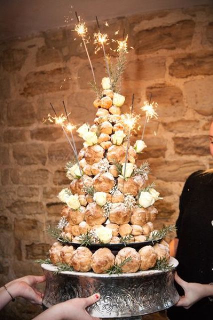 a cool croquembouche wedding cake topped with sugar powder, white roses, greenery and sparklers for a NYE wedding