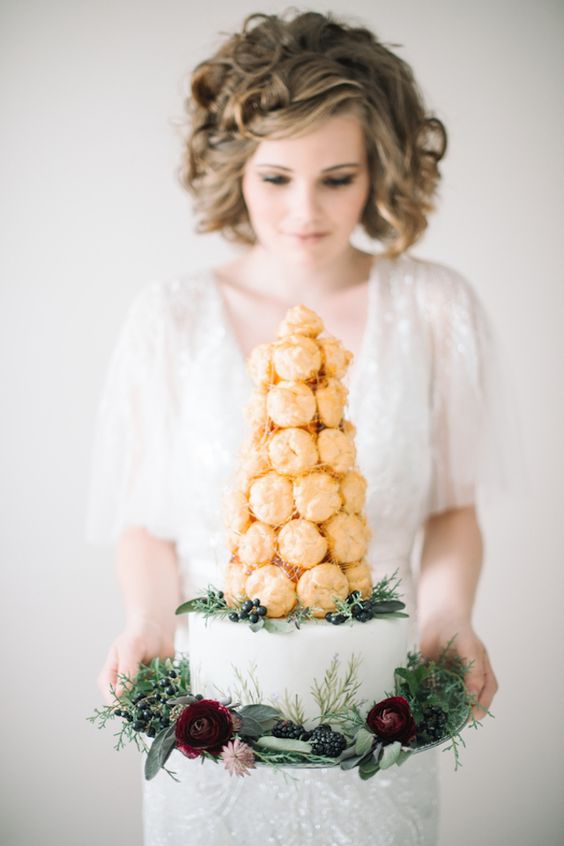 a cool wedding cake - a white one-tier cake and a croquembouche with sugar icing on top plus greenery and berries