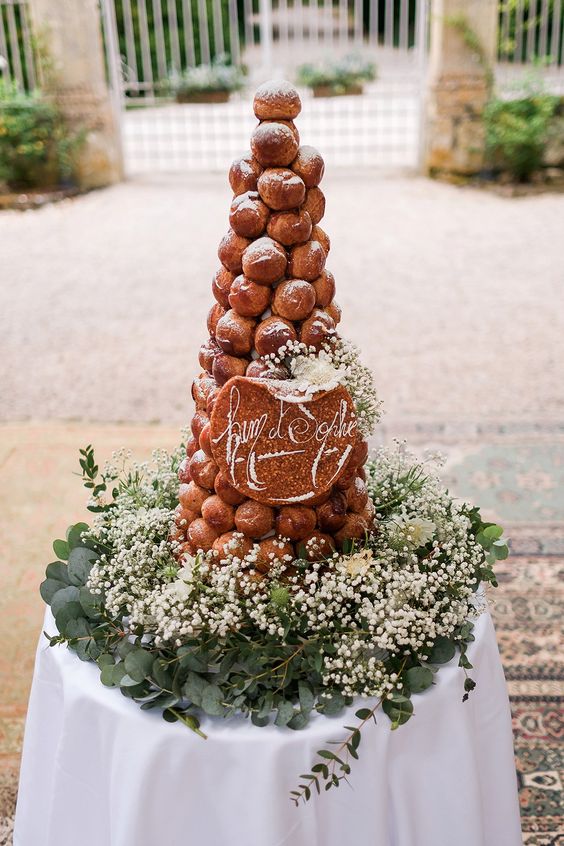 a croquembouche decorated with caramel and sugar powder, white baby's breath and a calligraphy topper
