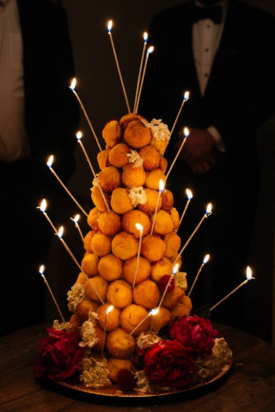 a croquembouche topped with tall and thin candles and some blooms plus caramel is a fantastic idea