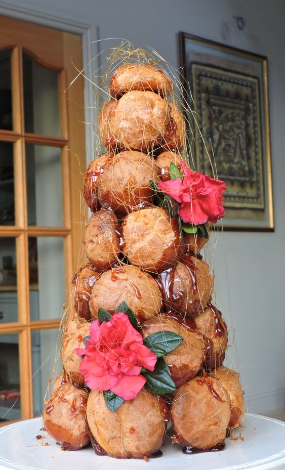 a croquembouche with caramel drip and sugar icing, with bold red blooms for a wedding with red color in the palette