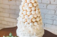 a dreamy white wedding cake covered with white blooms and topped with a wihte icing croquembouche plus a flower