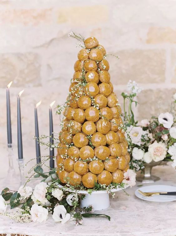 a glazed croquembouche decorated with blush blooms and blooming branches is a beautiful idea for a spring or summer wedding