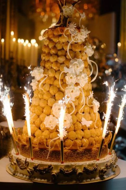 a large croquembouche decorated with white sugar blooms and swirls plus sparklers looks very party-like