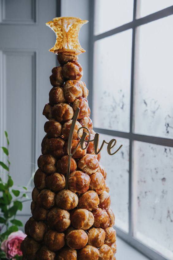 a large croquembouche topped with caramel drip, with a calligraphy topper and a creative caramel topper