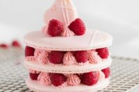 a large macaron cake with raspberries and raspberry cream, with a heart-shaped macaron and meringues on top