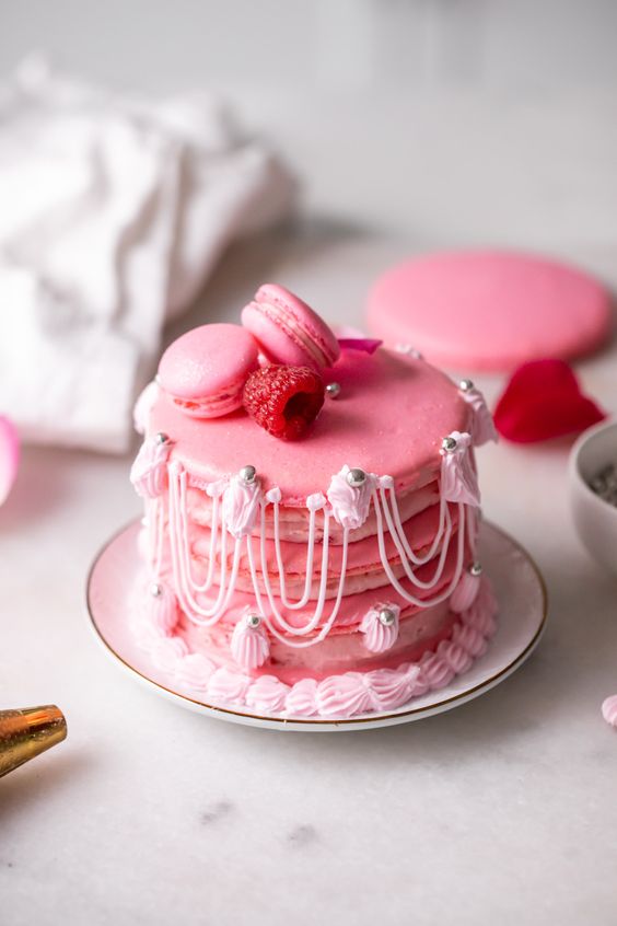 a large pink macaron wedding cake topped with mini macarons and a raspberry and whimsical detailing in Marie Antoinette style