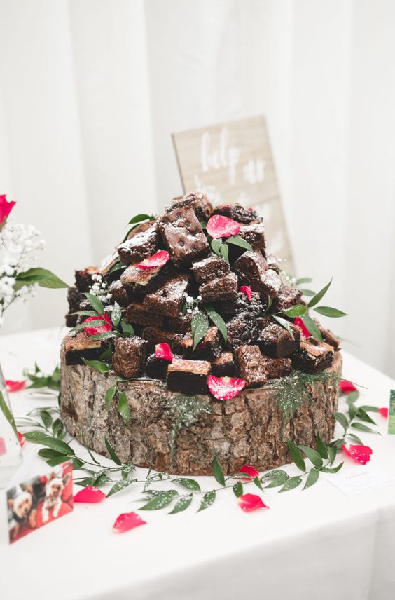 a large tree slice with brownies, pink flower petals, baby's breath and greenery on top is a cool idea for a rustic wedding