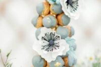 a pale blue croquembouche decorated with gold foil and large blooms is a gorgeous solution for a spring wedding