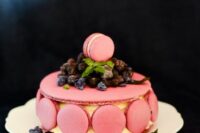a pink macaron cake with macarons on the side and lots of fresh berries on top is a refined and whimsical wedding cake idea