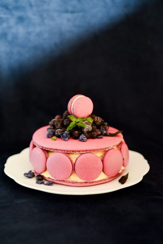 a pink macaron cake with macarons on the side and lots of fresh berries on top is a refined and whimsical wedding cake idea