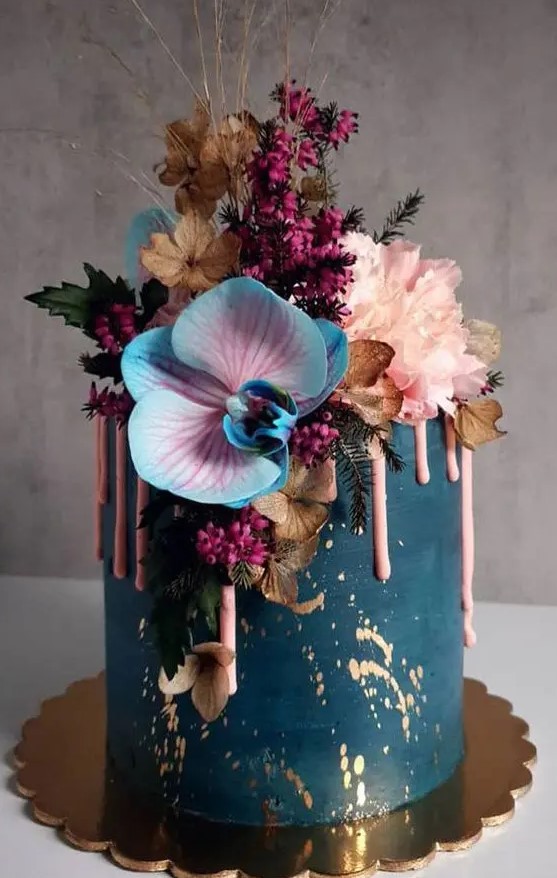 a refined and beautiful teal wedding cake with gold leaf and pink drip, with colorful blooms, berries and dried flowers and twigs