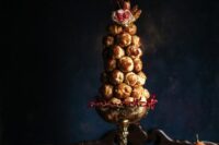 a refined croquembouche decorated with pink and red blooms and placed in a vintage bowl for a sophisticated wedding