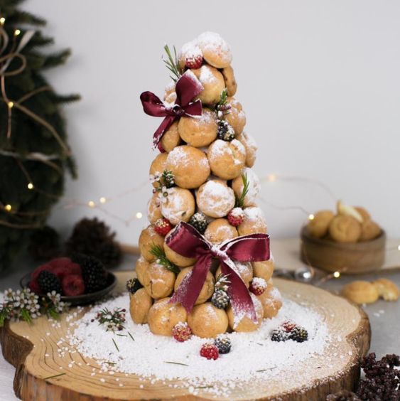 a small and cool croquembouche topped with sugar powder, with fresh berries and burgundy bows for a winter wedding