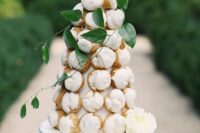 a small and elegant cied croquembouche decorated with white blooms and greenery is a lovely idea for a summer wedding